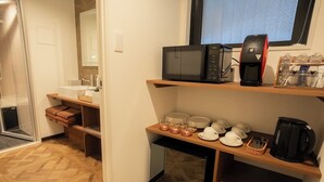A compact hotel room with a kitchenette, a small refrigerator, a microwave, a coffee maker, and a shelf with dishes and glasses. - XcellHIROSHIMA HEIWAODORI (Hiroshima)