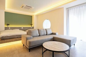A modern hotel room with a sectional sofa, a round coffee table, and a bed with a green accent wall. - XcellHIROSHIMA HEIWAODORI (Hiroshima)