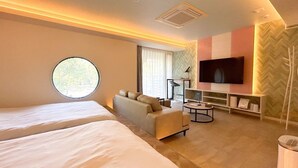 A hotel room with a large bed, a sofa, a TV, and a round window. - XcellHIROSHIMA HEIWAODORI (Hiroshima)