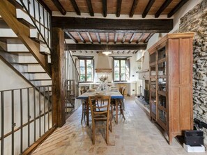 Un área de comedor con una mesa y sillas de madera, una escalera y una pared de piedra.