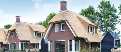 Una hilera de casas tradicionales con techos de paja, un césped y un canal al frente.