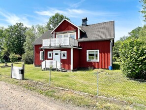 A two-story red house with a balcony, a fenced yard, and a clear sky.
