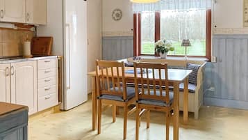 A kitchen with wooden cabinets, a white refrigerator, a dining table with four chairs, and a window with curtains.