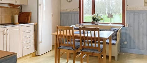 A kitchen with wooden cabinets, a white refrigerator, a dining table with four chairs, and a window with curtains.