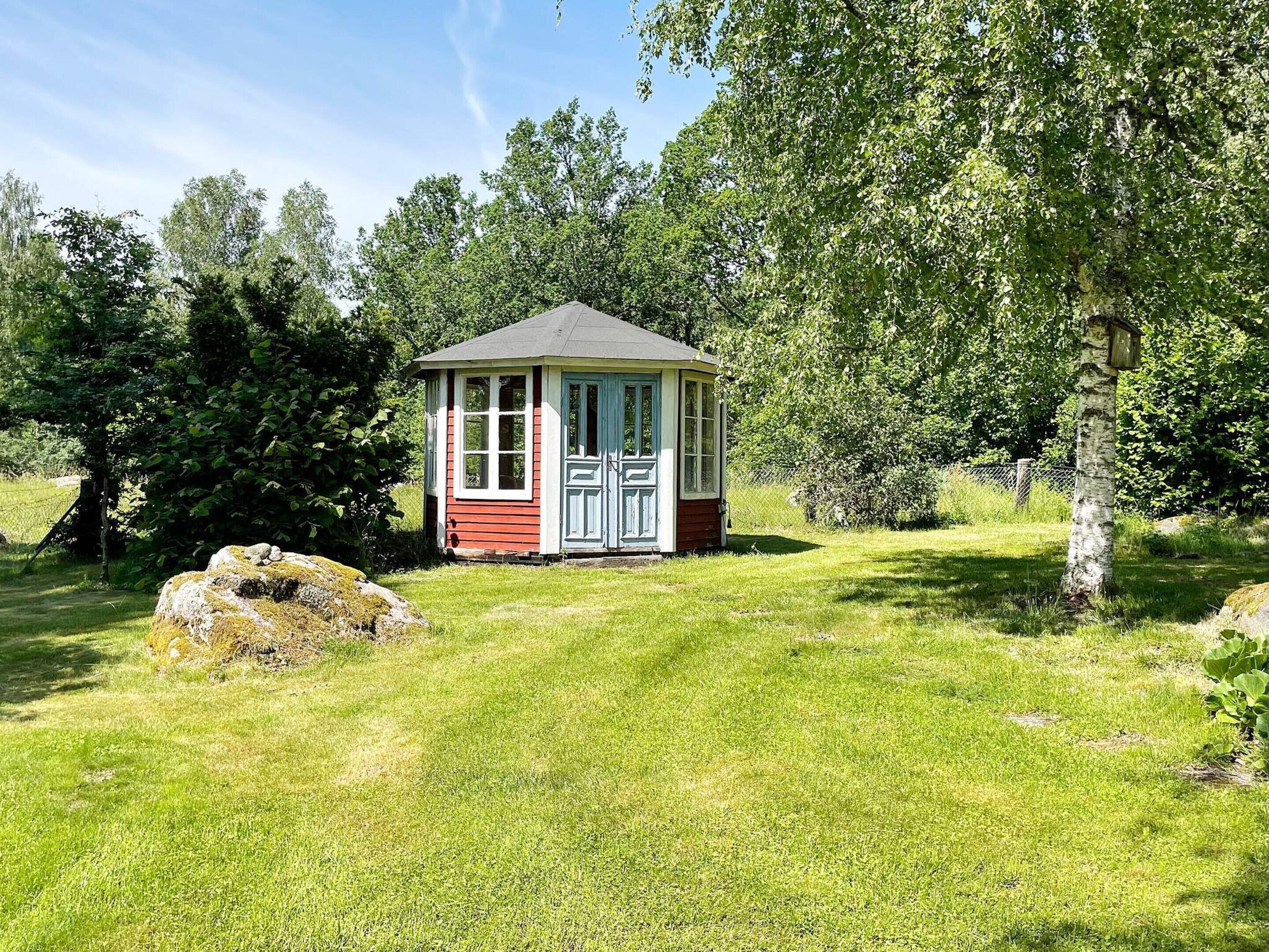 A small, single-story structure with a gabled roof, surrounded by lush greenery and trees.