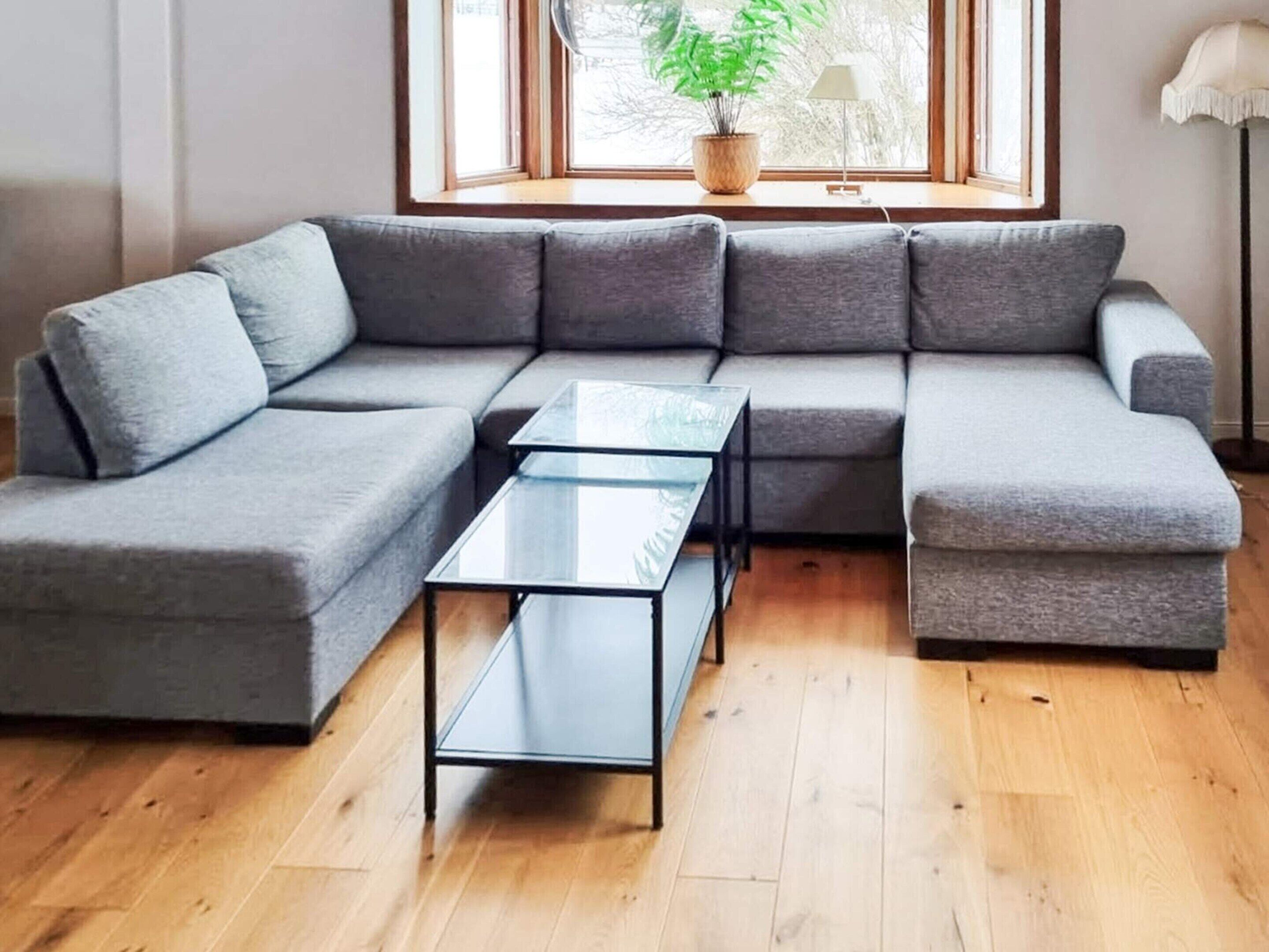 Een moderne woonkamer met een grijze modulaire bank, een glazen salontafel en een houten vloer.