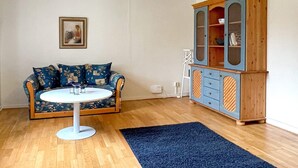 A room with a blue patterned sofa, a white round table, a wooden cabinet with glass doors, and a yellow pendant light. - 7 Person Holiday Home in Hogsby (Högsby)