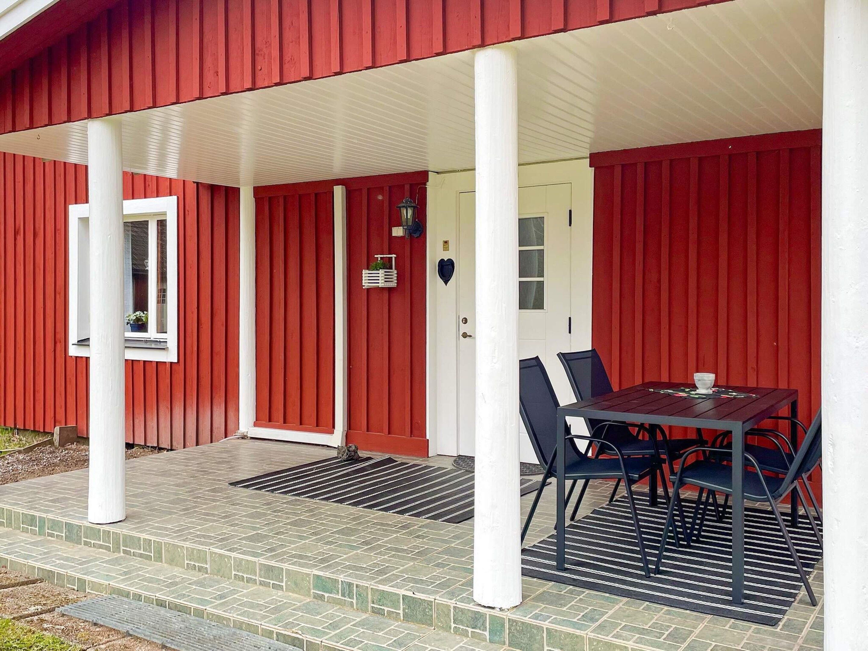 A red building with a covered porch, a table with chairs, and a door with a window.