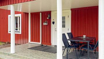 A red building with a covered porch, a table with chairs, and a door with a window.