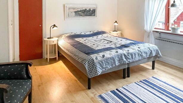 A bedroom with a bed, two bedside tables, a chair, a window with curtains, and a picture on the wall. - 7 Person Holiday Home in Hogsby (Högsby)