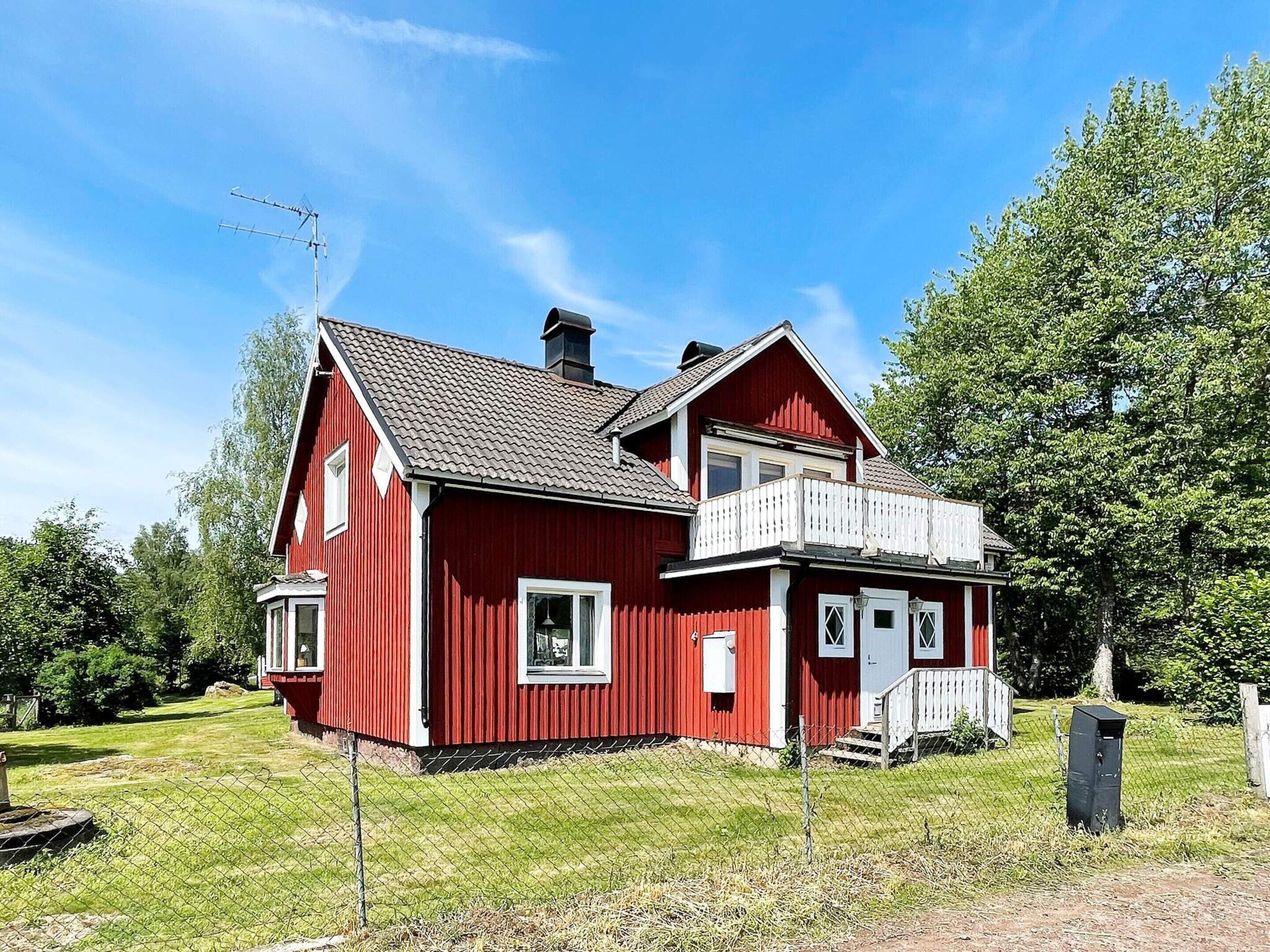 A red two-story house with a balcony, a chimney, and a fenced yard.