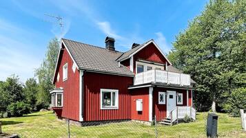 A red two-story house with a balcony, a chimney, and a fenced yard.