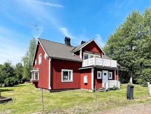 A red two-story house with a balcony, a chimney, and a fenced yard. - 7 Person Holiday Home in Hogsby (Högsby)