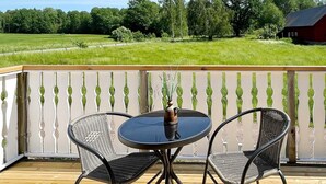 Eine Holzterrasse mit einem runden Tisch und zwei Stühlen, mit Blick auf ein saftiges Grasfeld und eine rote Scheune.