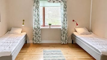 A room with two single beds, a window with curtains, a hanging light fixture, and a small plant on the windowsill.