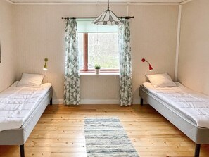 A room with two single beds, a window with curtains, a hanging light fixture, and a small plant on the windowsill. - 7 Person Holiday Home in Hogsby (Högsby)
