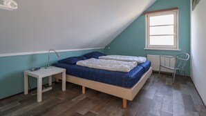 Una stanza piccola e luminosa con soffitto a falde, un letto con biancheria azzurra, un comodino con una lampada e un termosifone.