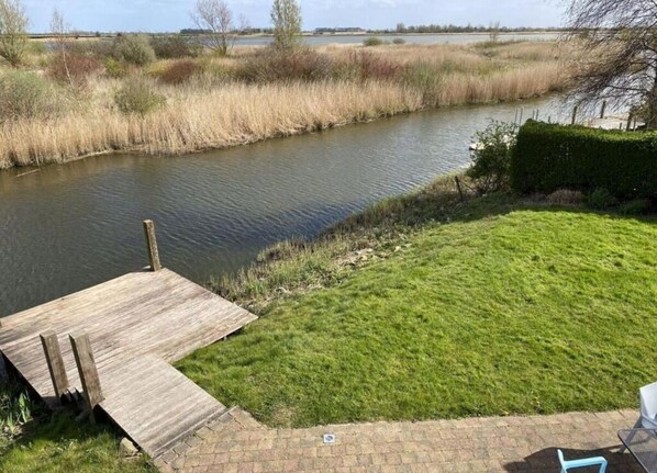 Vista al río con césped y un muelle de madera.
