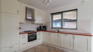 Cucina con mobili bianchi, un fornello, un forno, un lavello e una finestra con persiane.
