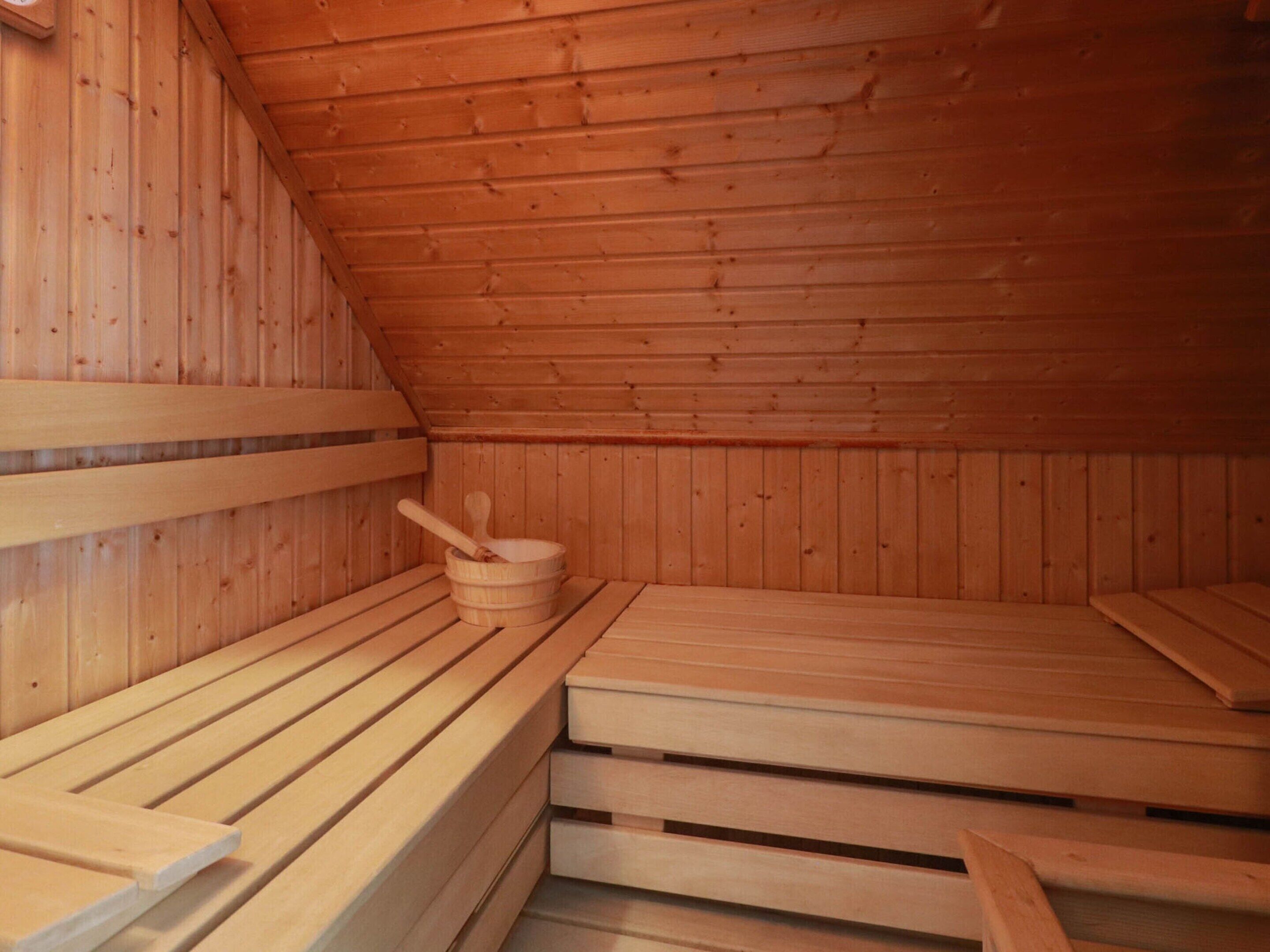 Una sala de sauna con bancos de madera y un balde de madera con una cuchara.