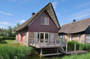 Ein Haus mit einem Strohdach, einer Holzterrasse und einem Teich davor.