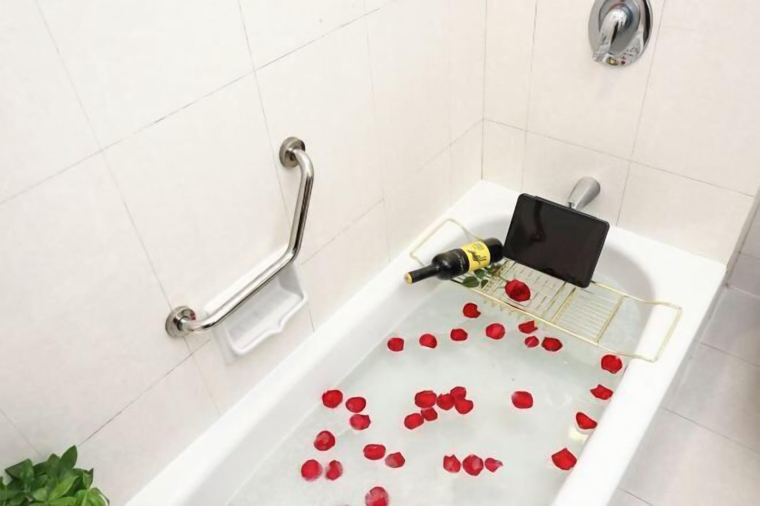 Eine Badewanne mit Rosenblättern, einer Flasche, einer Handstange und einer Pflanze.