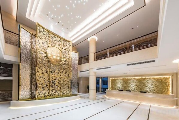 Un hall d’entrée spacieux avec un plafond haut, un mur décoratif orné de motifs complexes et un luminaire moderne.