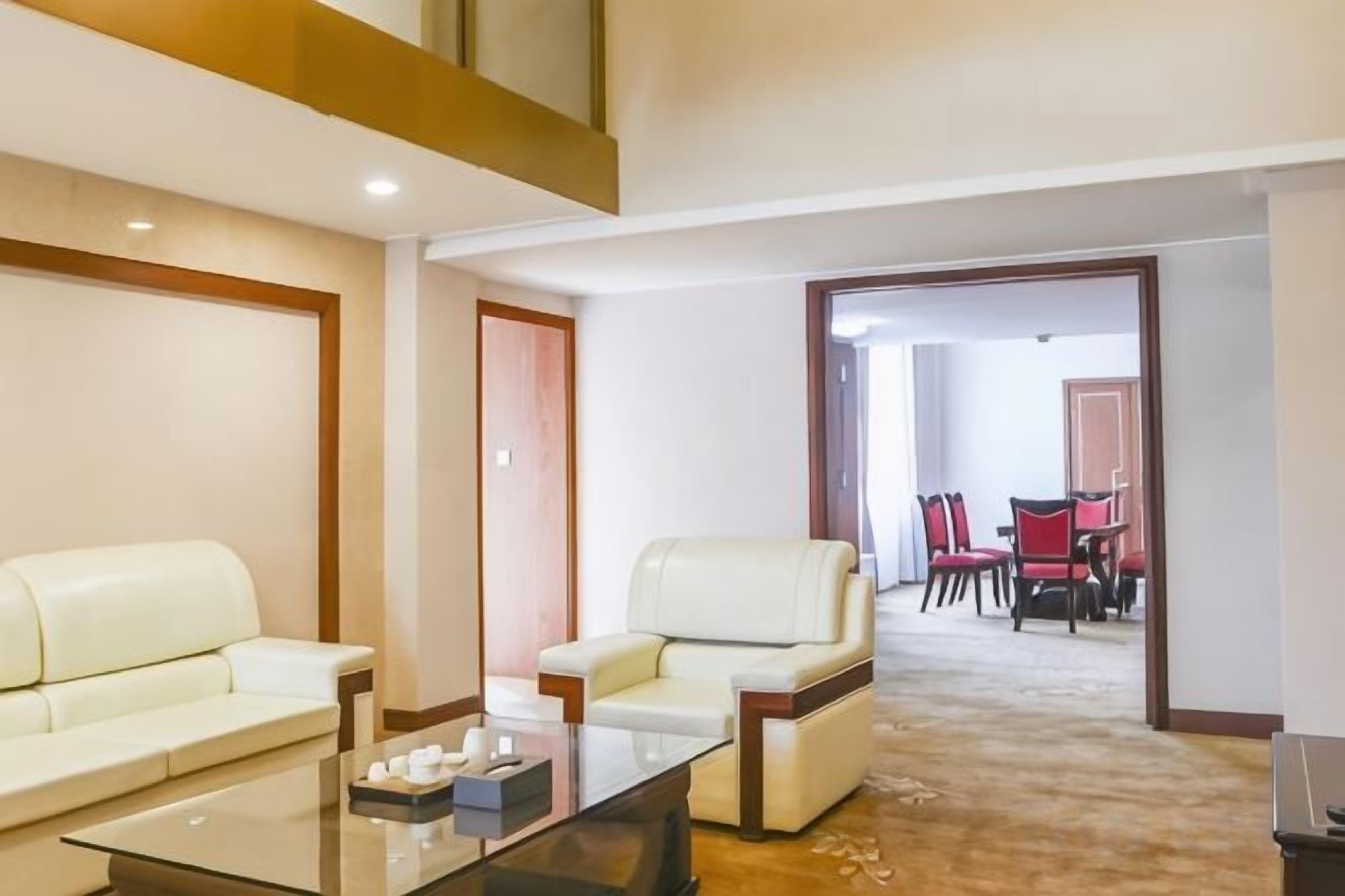 Habitación de hotel con sofá, sillón y comedor con sillas y mesa.