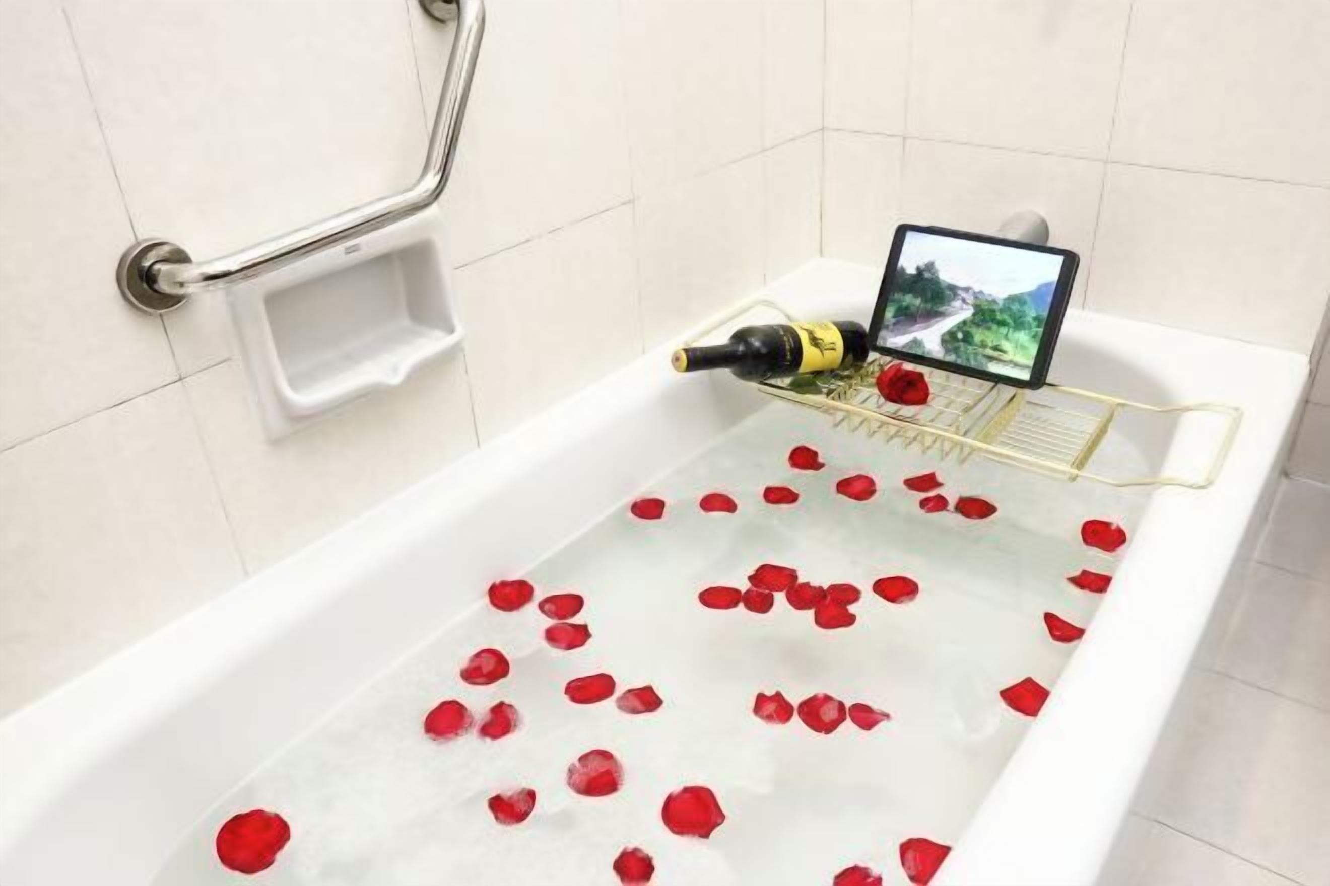 A bathtub with rose petals, a bottle, and a tablet.
