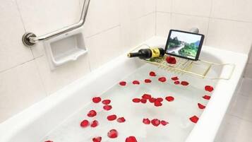 A bathtub with rose petals, a bottle, and a tablet.