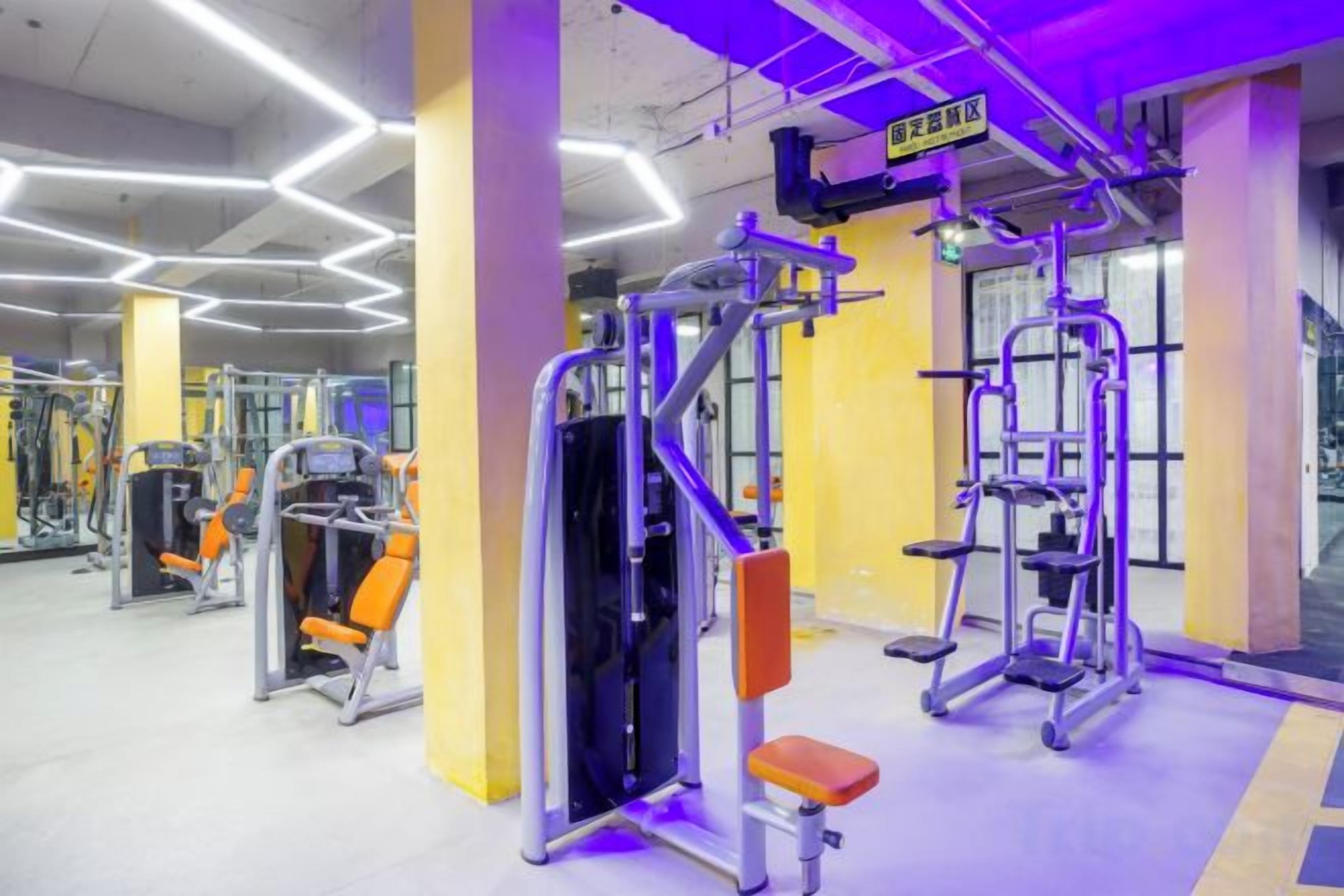 Une salle de sport équipée de divers appareils d’exercice, d’un banc et d’un panneau indiquant la zone dédiée à la musculation.