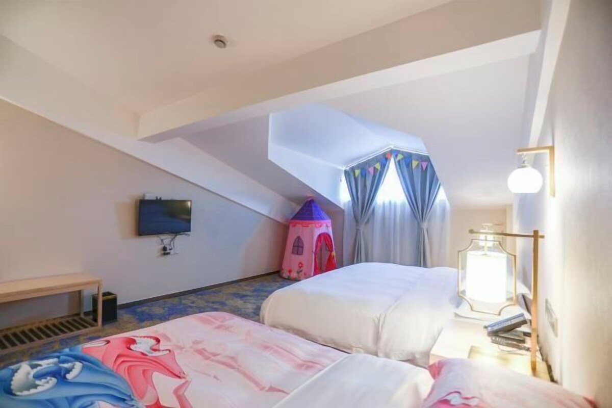 A bedroom with two beds, a small table, a lamp, and a TV on the wall.
