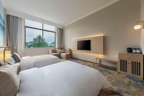 A hotel room with two beds, a TV, a desk with a coffee maker, and a view of the outdoors.
