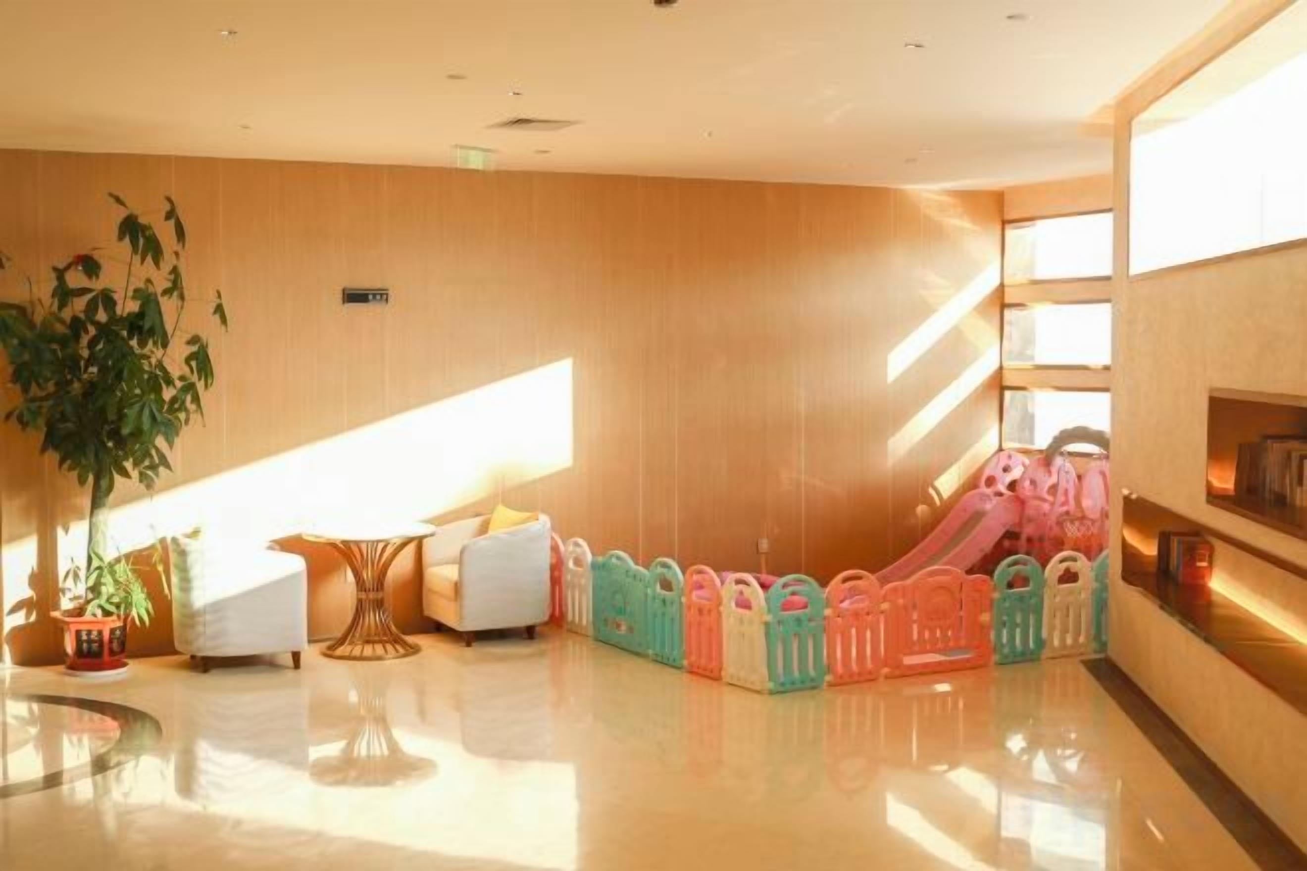 Um hall de hotel moderno com área de recreação infantil, uma grande planta em vaso e um espaço de estar com sofá e mesa.