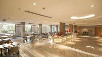 En rummelig hotellobby med en central receptionsdisk, flere siddeområder og store vinduer der lukker naturligt lys ind.