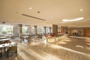 Un hall d’hôtel spacieux, doté d’un comptoir d’accueil central, de plusieurs espaces de détente et de grandes fenêtres laissant entrer la lumière naturelle.