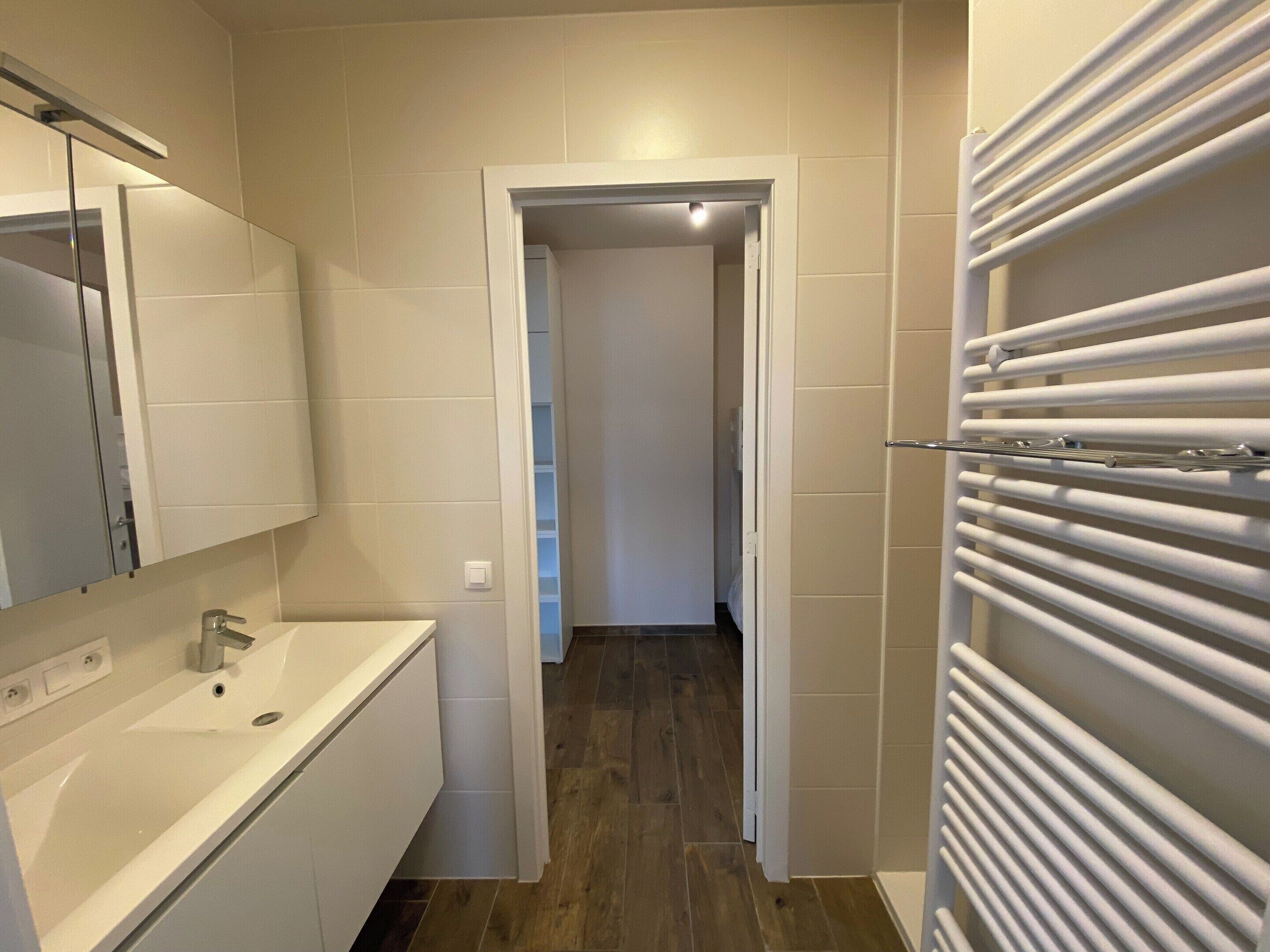 A modern bathroom with a white sink, mirror, and a towel rack.