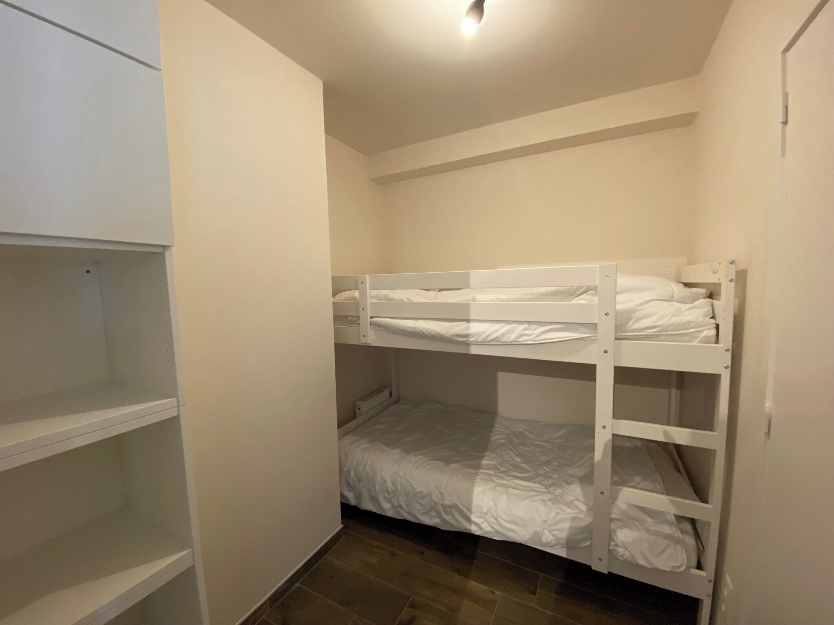 Une chambre avec un lit superposé, une armoire blanche et un sol carrelé.