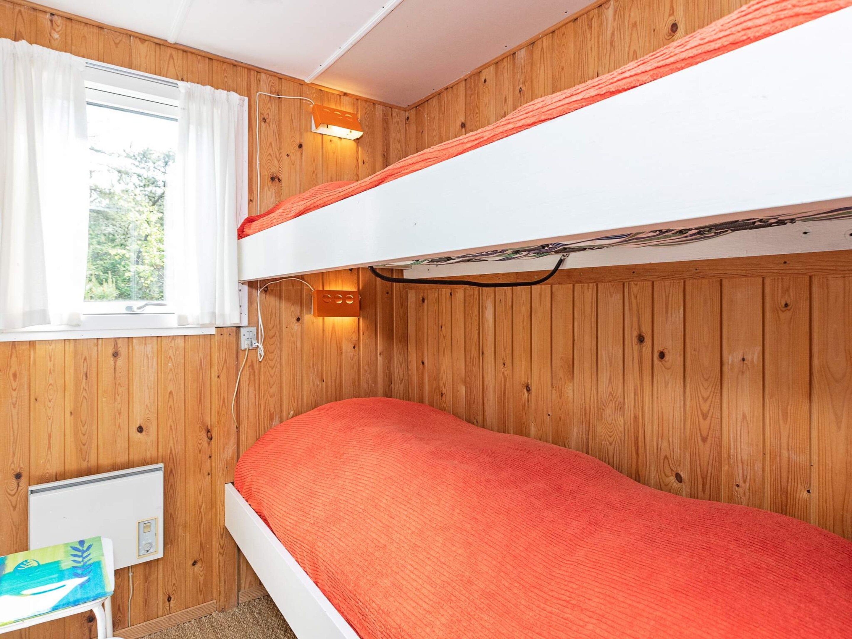 A bunk bed room with wooden paneling, a window with curtains, and a small table with a colorful item on it.