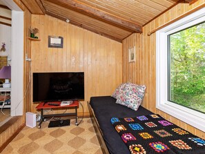 A cozy room with wooden walls, a bed with a colorful blanket, a television on a stand, and a window with a view of trees. - 4 Person Holiday Home in Blokhus (Blokhus)