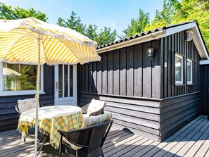 A wooden deck with a table and chairs under a striped umbrella, a door, and a window.