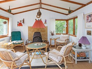 A cozy room with wicker furniture, a fireplace, and large windows. - 4 Person Holiday Home in Blokhus (Blokhus)