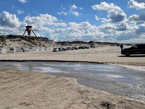 A sandy beach with a row of beach huts and a tall structure on a hill. - 4 Person Holiday Home in Blokhus (Blokhus)
