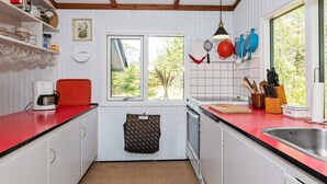 A kitchen with white cabinets, a red countertop, a window with a view, and various kitchen utensils. - 4 Person Holiday Home in Blokhus (Blokhus)
