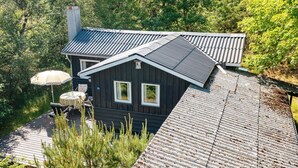 A dark wooden house with a sloped roof, a chimney, and a deck with outdoor furniture. - 4 Person Holiday Home in Blokhus (Blokhus)