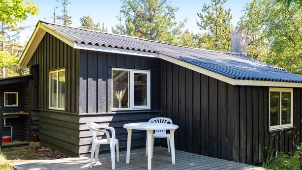 A wooden cabin with a deck, two chairs, and a table. - 4 Person Holiday Home in Blokhus (Blokhus)