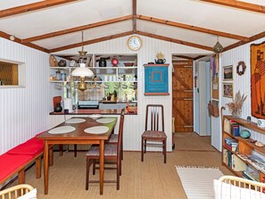A cozy, rustic kitchen with wooden beams, a dining table with chairs, and a bookshelf filled with books and decorative items. - 4 Person Holiday Home in Blokhus (Blokhus)
