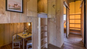 Un interior de madera con una cama litera, una mesa con sillas y un cuadro en la pared.