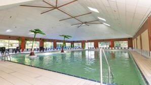 Una piscina interior con agua cristalina, rodeada de paredes de azulejos y un techo alto con vigas de madera.
