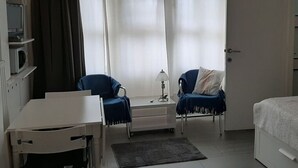 Ein Hotelzimmer mit einem Bett, einem Schreibtisch, zwei Stühlen, einer Lampe und einem großen Fenster mit Vorhängen.